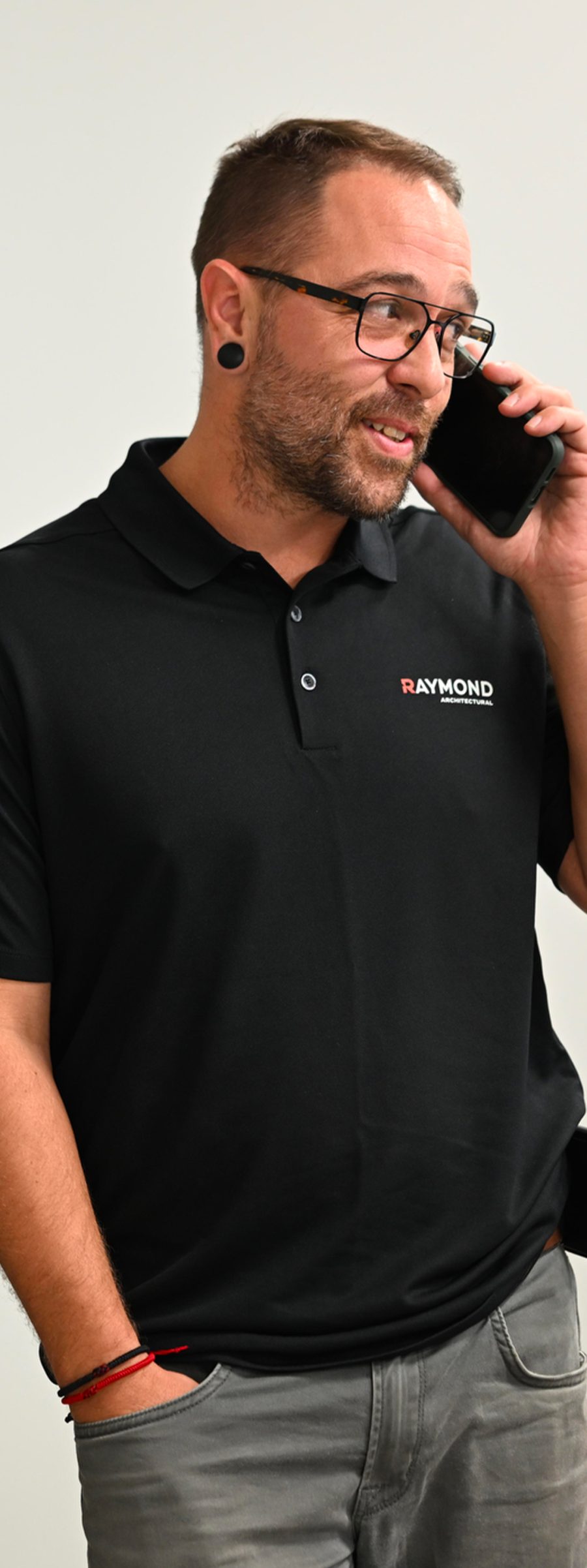Employé de Raymond Architectural en polo corporatif noir discutant au téléphone pour le service client et la gestion de projets – Raymond Architectural