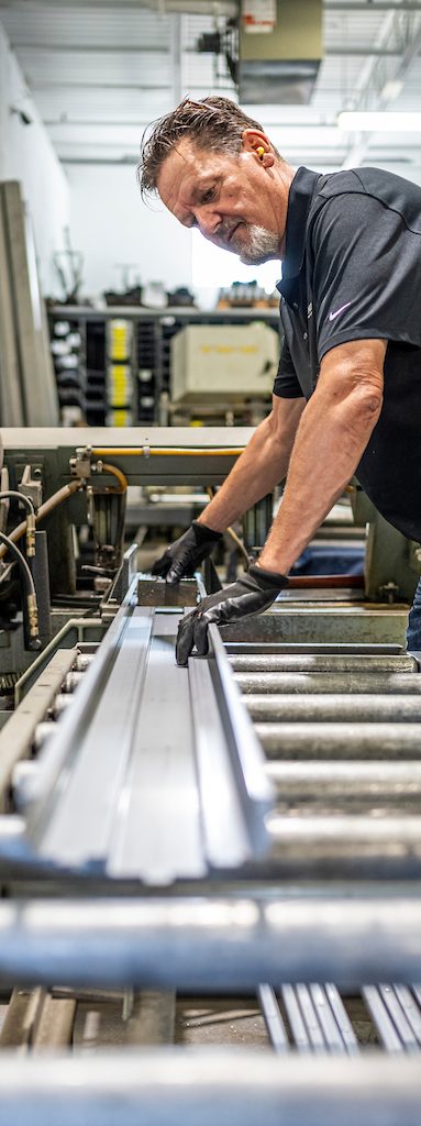 Employé de Raymond Architectural en atelier manipulant des profilés métalliques pour la fabrication de cadres en acier – Raymond Architectural