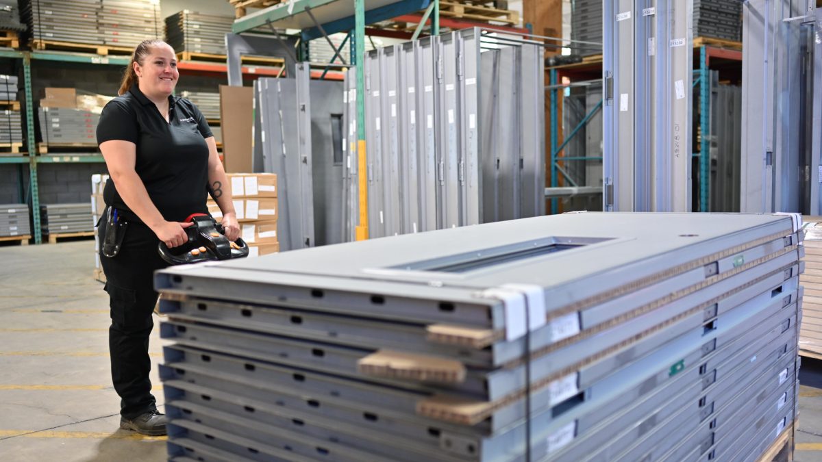 Employée de Raymond Architectural déplaçant une pile de portes en acier dans l’atelier de fabrication – Raymond Architectural