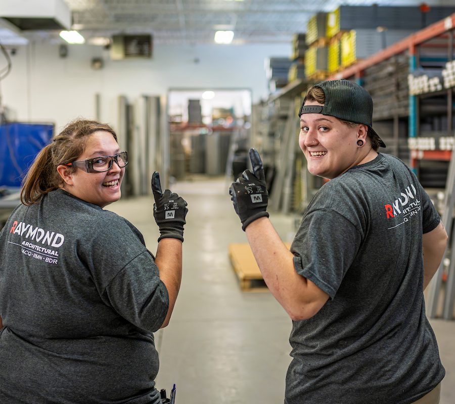 Deux employés de Raymond Architectural souriants dans l’atelier de fabrication de portes et cadres en acier – Raymond Architectural