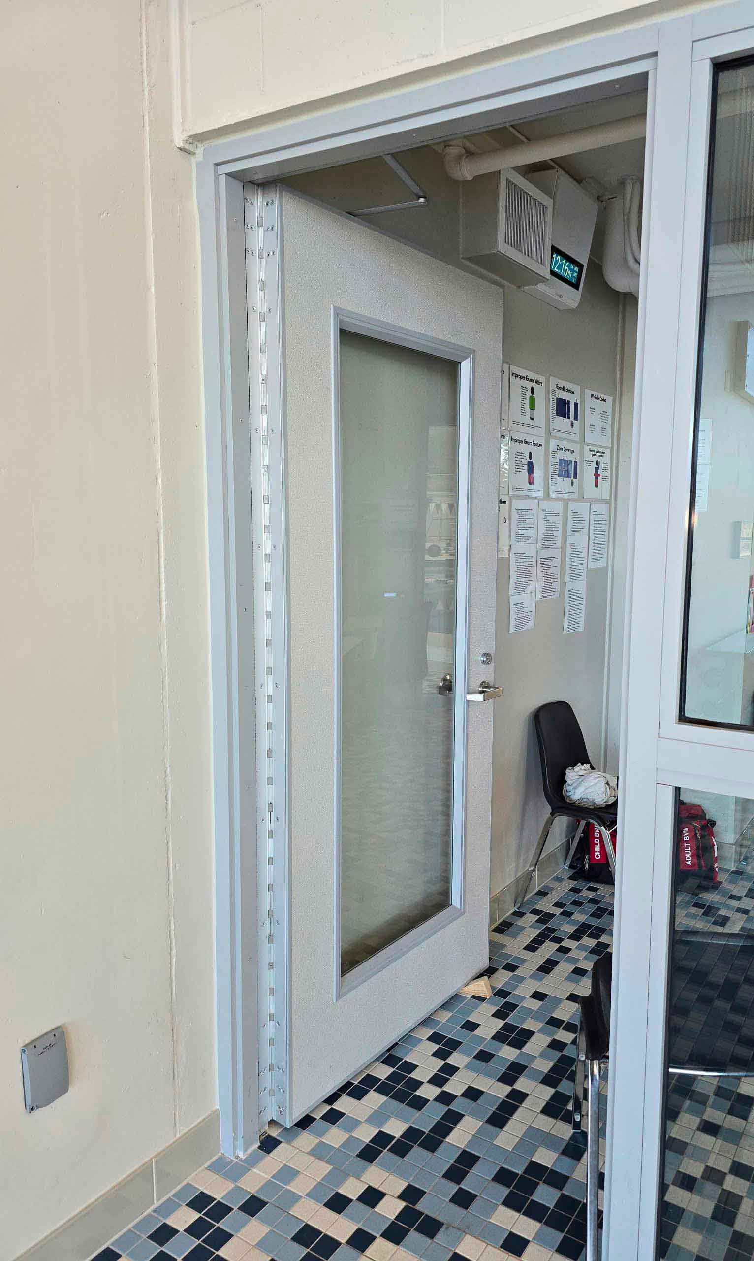 Porte intérieure vitrée avec cadre métallique clair dans un environnement institutionnel moderne – Raymond Architectural