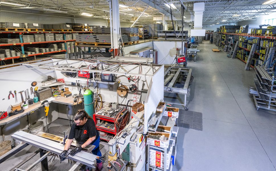 Vue d’ensemble de l’atelier de Raymond Architectural avec un employé travaillant sur des profilés métalliques pour la fabrication de portes et cadres en acier – Raymond Architectural
