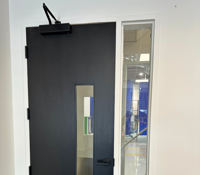 Porte architecturale en acier noir avec ouverture vitrée et imposte latérale dans un bâtiment moderne – Raymond Architectural