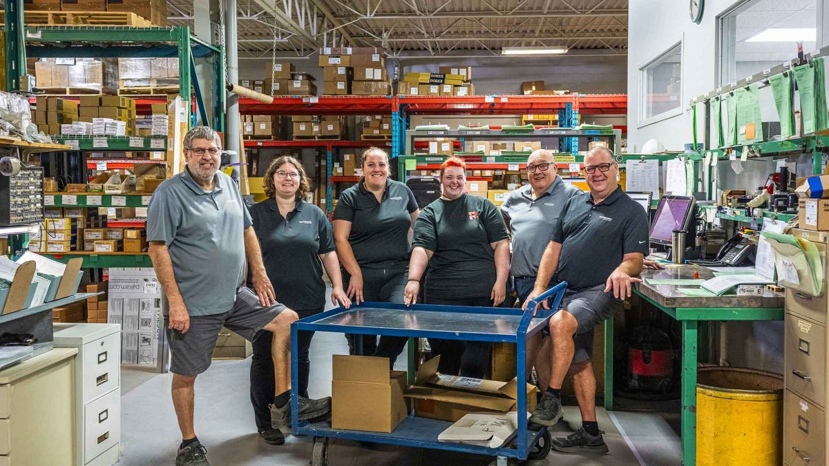 Équipe d’employés de Raymond Architectural posant ensemble dans l’entrepôt logistique de portes, cadres et quincaillerie – Raymond Architectural